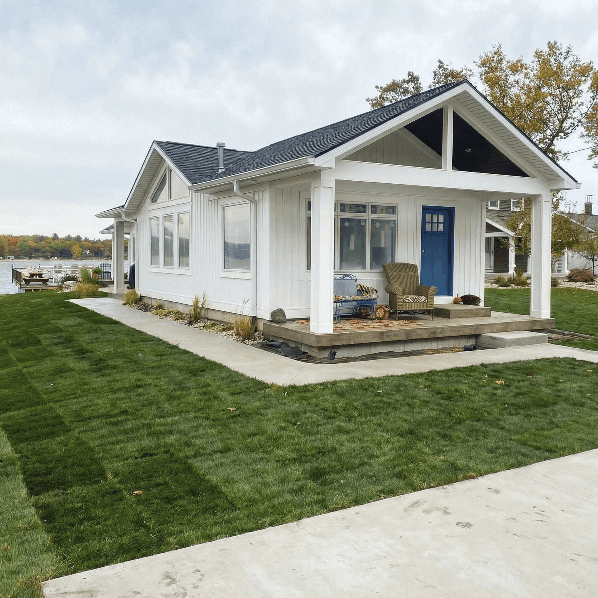 Charming white lakeside cottage remodel in Michigan with fresh siding, blue front door, covered porch, and new sod installation